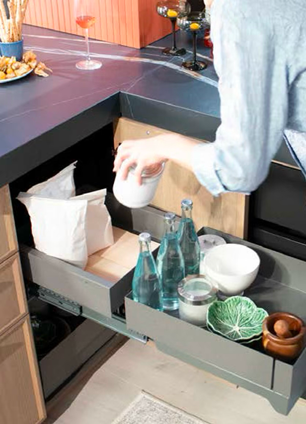 La imagen muestra una persona colocando una taza en un cajón de cocina. Este espacio cuenta con muebles funcionales, como un mostrador elegante y una variedad de utensilios, que hacen la cocina práctica y acogedora.