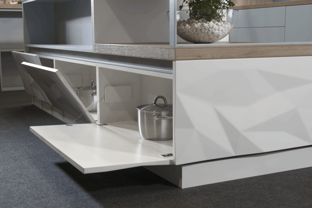 Módulo inferior con puertas abatibles, diseño en acabado blanco brillante con relieve facetado. Interior espacioso y funcional, ideal para almacenar utensilios de gran tamaño. Encimera en madera clara que aporta calidez y contraste.