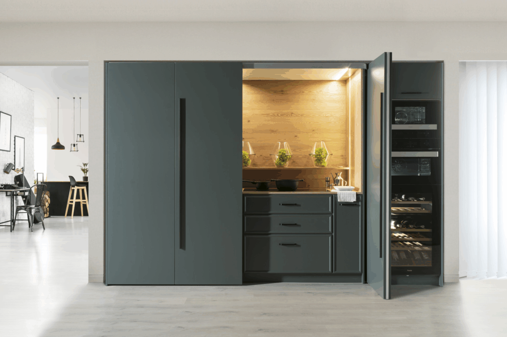 Cocina oculta de diseño elegante, con mobiliario en gris oscuro mate y sistema de apertura discreto. El interior en madera clara crea un efecto cálido y natural, realzado por la iluminación led integrada. Práctica y estilizada, se adapta perfectamente a espacios modernos donde cada rincón cuenta.