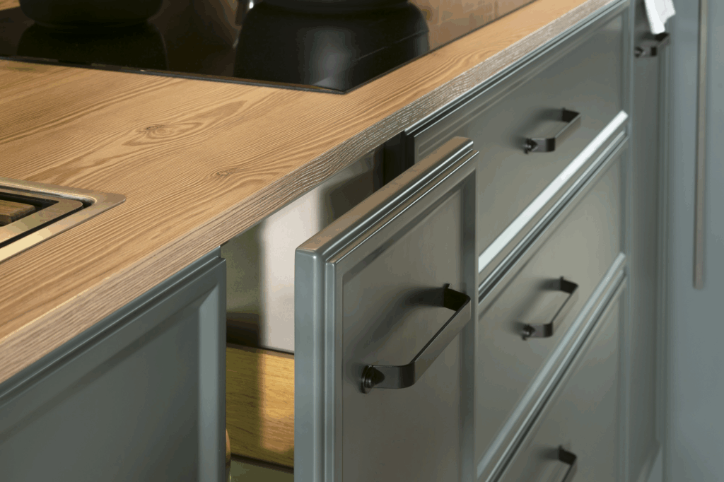 Detalle de cocina con muebles en gris grafito y acabado mate, rematados con tiradores negros metálicos. La encimera de madera natural aporta calidez y contraste al conjunto, mientras que la organización interior revela soluciones funcionales y elegantes para el almacenaje.