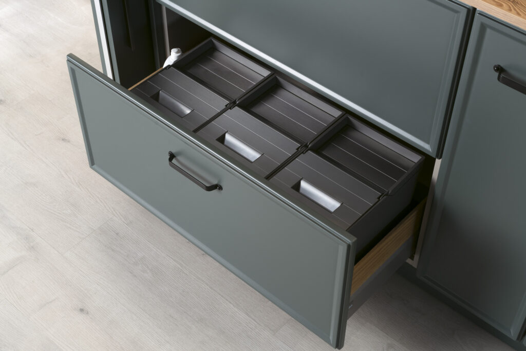 Cajón bajo con tres contenedores modulares perfectamente encajados, ideal para reciclaje o almacenaje. El acabado en gris oscuro mantiene la estética sobria y elegante del conjunto.