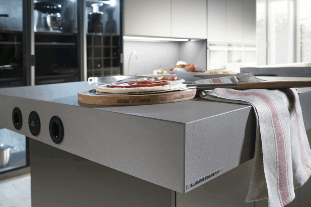 Isla de cocina con encimera robusta en acabado Laminam, que incorpora tomas eléctricas empotradas. Diseño pensado para la acción: funcional, resistente y listo para inspirar cada preparación.