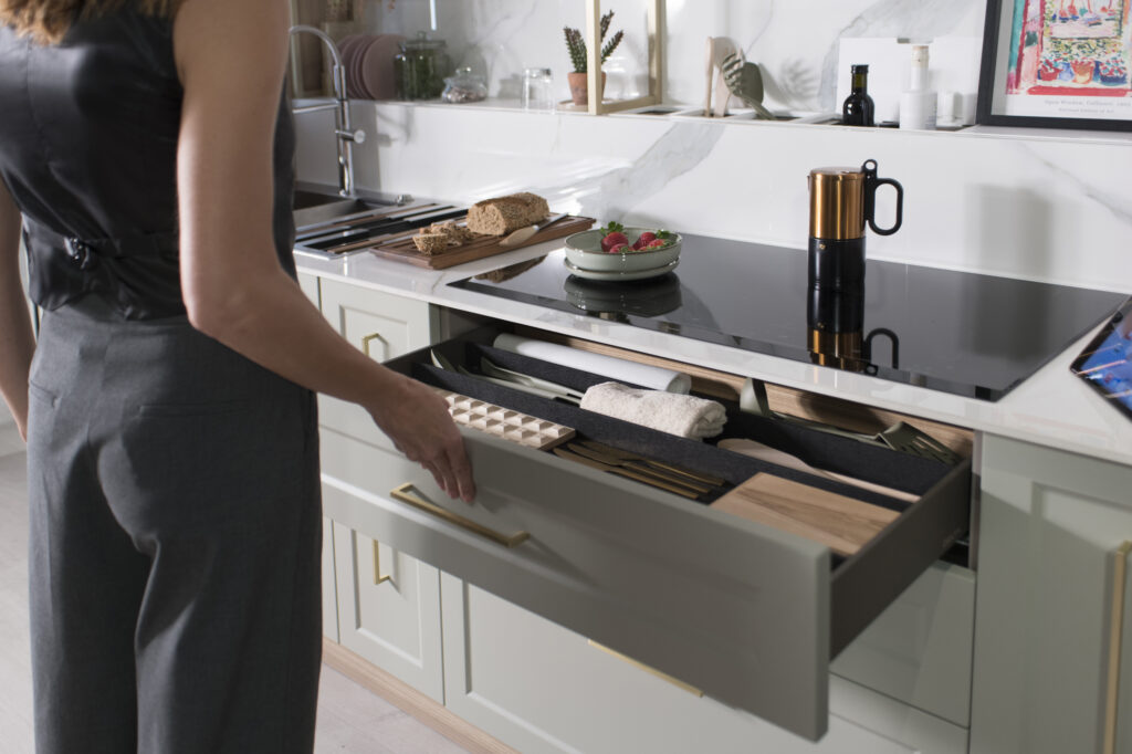 Cajón amplio y bien organizado con divisores para utensilios, rodillos y tablas de corte. Parte de una cocina de diseño elegante con acabados en verde salvia y mármol. Funcionalidad y estilo en perfecta armonía.