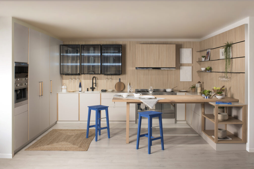En esta cocina se destaca una mesa central rodeada de taburetes azules, creando un ambiente acogedor. Los acabados en los muebles y la combinación de colores aportan un toque moderno y funcional al espacio.