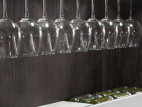 Vasos de vino elegantes ubicados en una estantería moderna, con un diseño transparente que complementa el entorno. A su lado, una botella de vino aporta un toque artístico y sofisticado a la decoración interior.