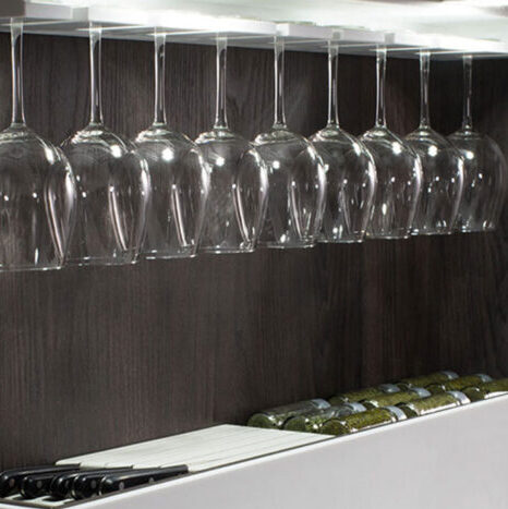 Vasos de vino elegantes ubicados en una estantería moderna, con un diseño transparente que complementa el entorno. A su lado, una botella de vino aporta un toque artístico y sofisticado a la decoración interior.