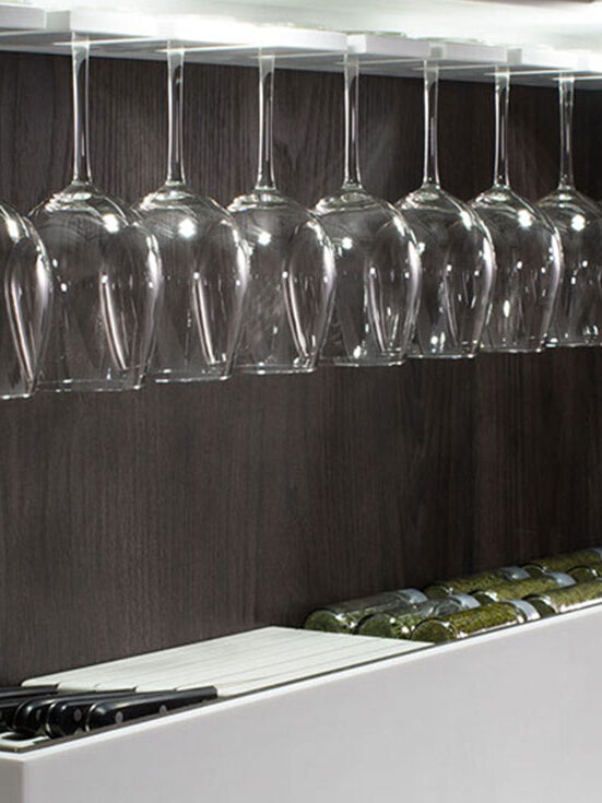 Copas colgantes que reflejan la luz con elegancia, acompañadas por botellas y utensilios perfectamente alineados: un rincón sofisticado que invita a disfrutar del arte de servir con estilo.