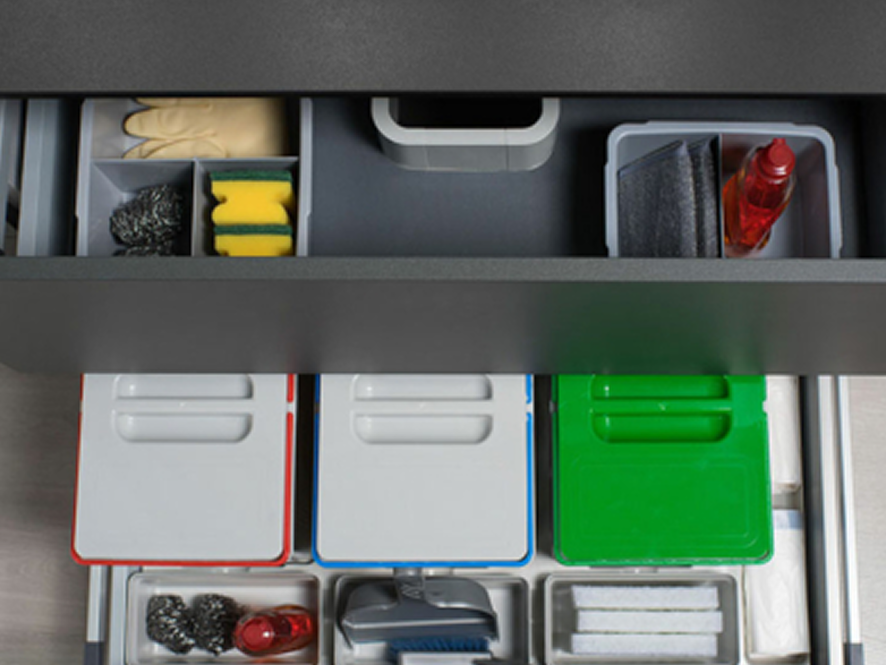 Un cajón diseñado para la eficiencia: contenedores de reciclaje codificados por color y compartimentos organizados para guantes, esponjas y productos de limpieza, todo en un solo lugar, oculto y accesible.