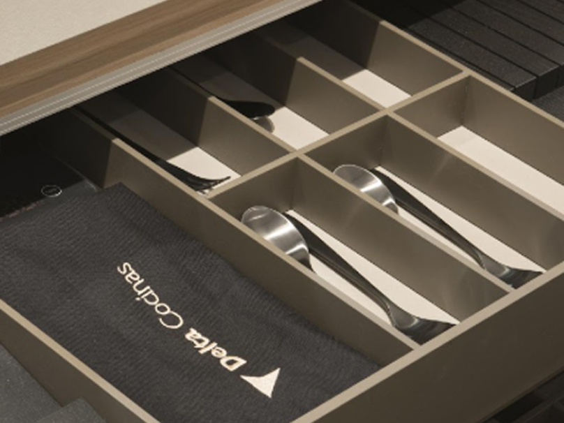 Elegancia en cada detalle: cajón con separadores refinados que ordenan la cubertería con precisión, complementado con textiles y accesorios que realzan la experiencia en la cocina.