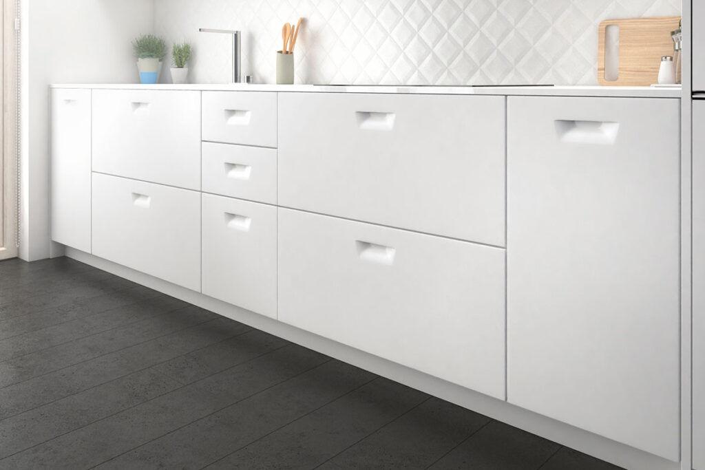 Cocina de estilo minimalista con mobiliario blanco mate y tiradores integrados. El diseño lineal y los frentes lisos refuerzan la sensación de orden y amplitud, mientras el suelo oscuro y el revestimiento texturizado en la pared aportan contraste y elegancia.