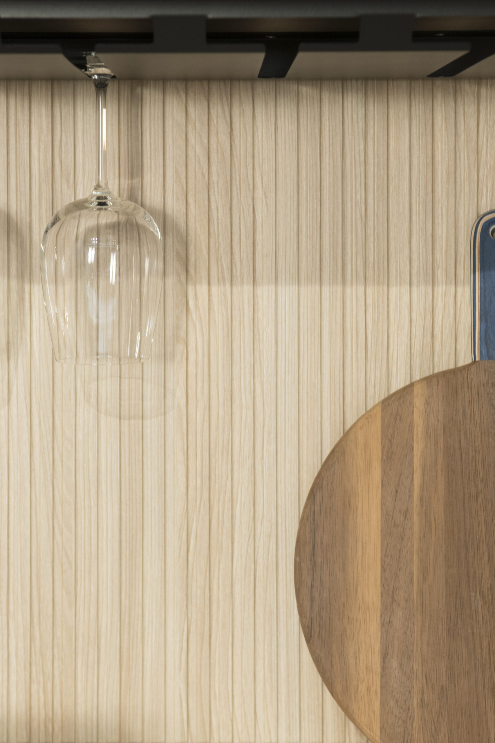 Una copa de cristal se mece suspendida sobre un fondo de listones de madera clara, capturando destellos de luz y sugerencias de calidez. Su delicada silueta invita a imaginar brindis íntimos y momentos de pausa, donde cada detalle aporta armonía y serenidad al espacio.